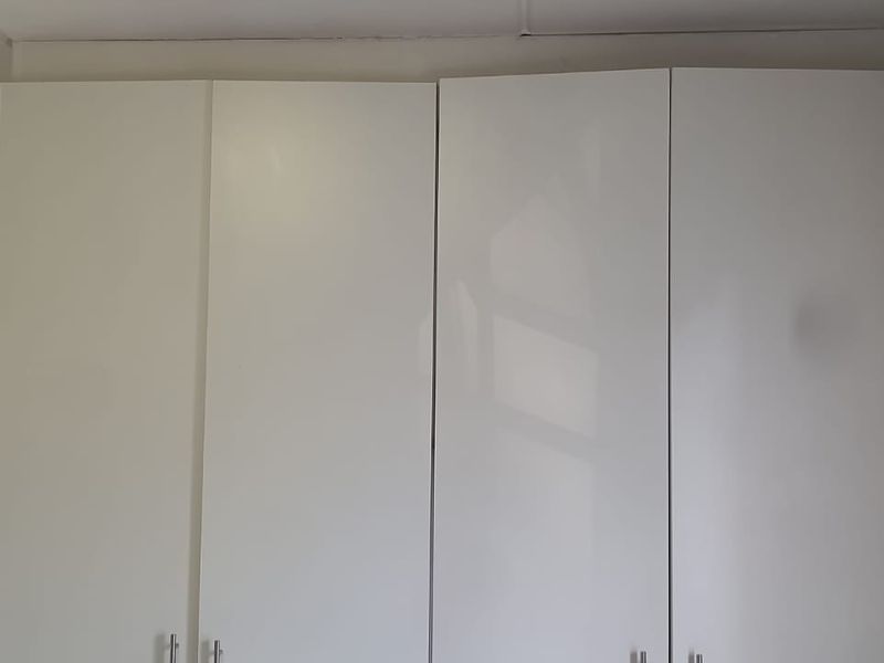 A bedroom featuring white built-in cupboards with simple hardware, showing signs of basic installation and finish.