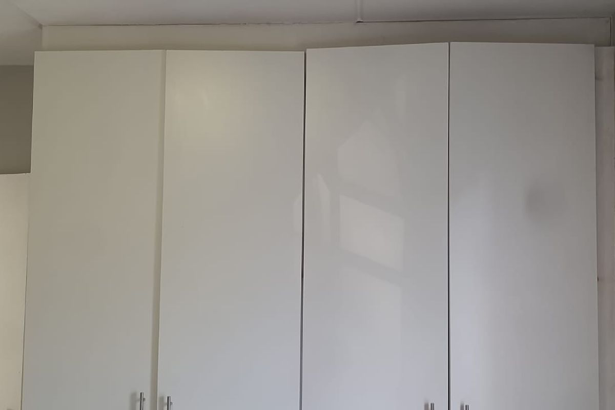 A bedroom featuring white built-in cupboards with simple hardware, showing signs of basic installation and finish.