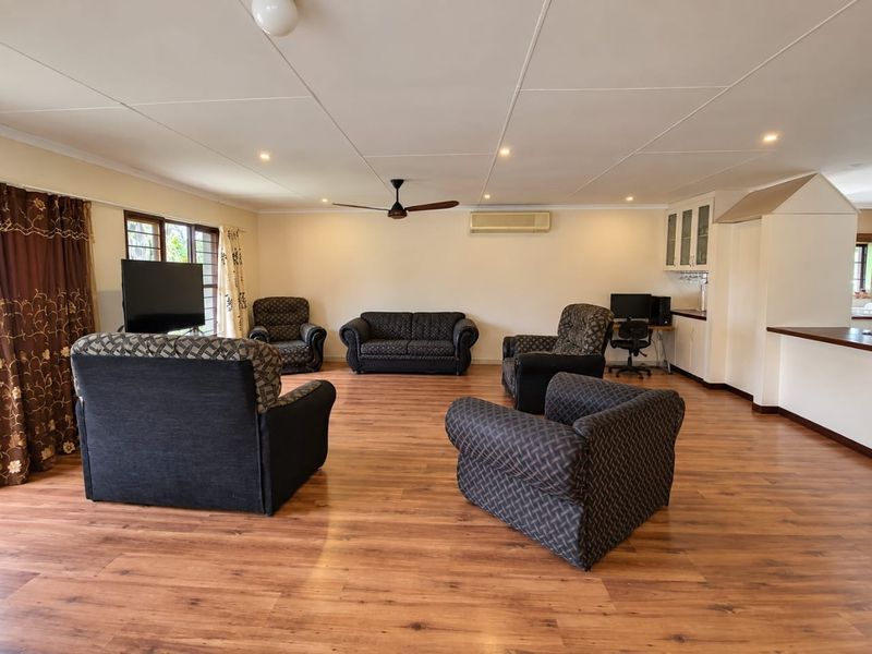 Spacious open-plan living area featuring laminate flooring, a ceiling fan, split system air conditioning, and integrated cabinetry with a breakfast bar.