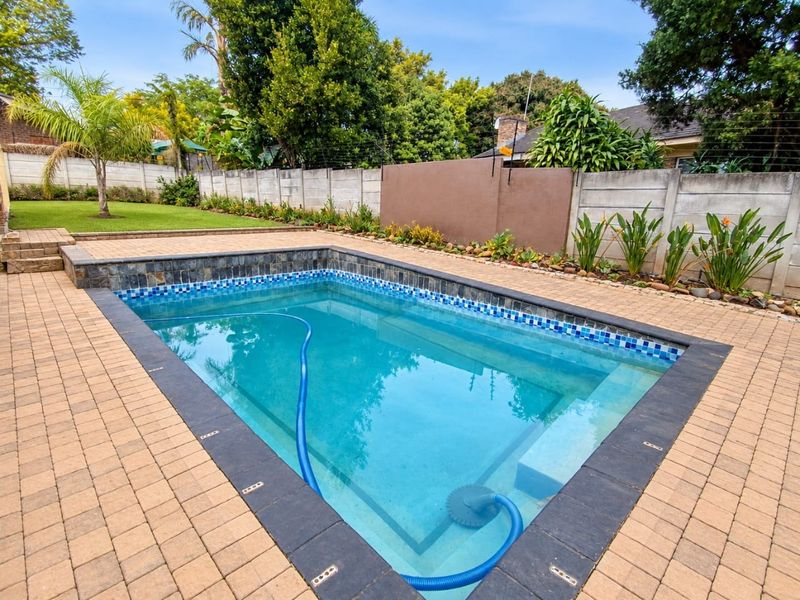 A well-maintained swimming pool area featuring a paved deck, landscaped garden, and secure perimeter walling with electric fencing.