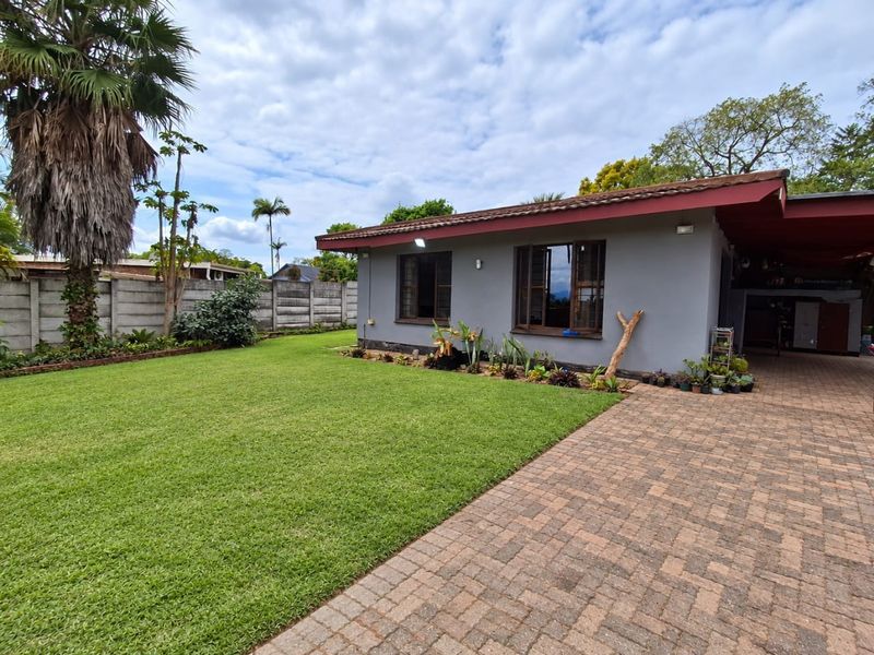 A well-maintained rear exterior view featuring a paved driveway, a spacious lawn, and a solid concrete boundary wall.