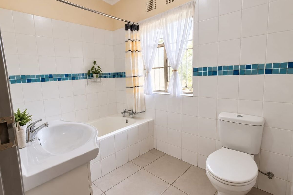 A functional bathroom featuring a bathtub, pedestal basin, and toilet, finished with white wall tiles and a decorative blue accent border.