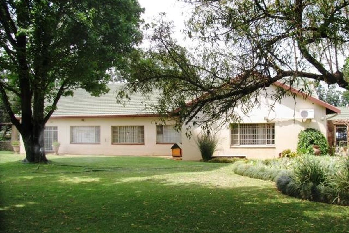 Rear view of the farm property featuring a well-maintained lawn, mature trees, and a single-story building with tiled roofing and security window bars.