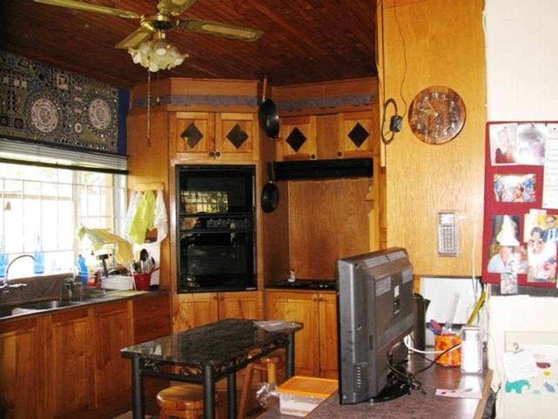 A dated kitchen featuring extensive wooden cabinetry, built-in oven and hob, and a wooden ceiling, offering significant potential for a modern renovation.