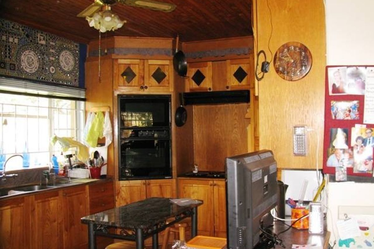 A dated kitchen featuring extensive wooden cabinetry, built-in oven and hob, and a wooden ceiling, offering significant potential for a modern renovation.