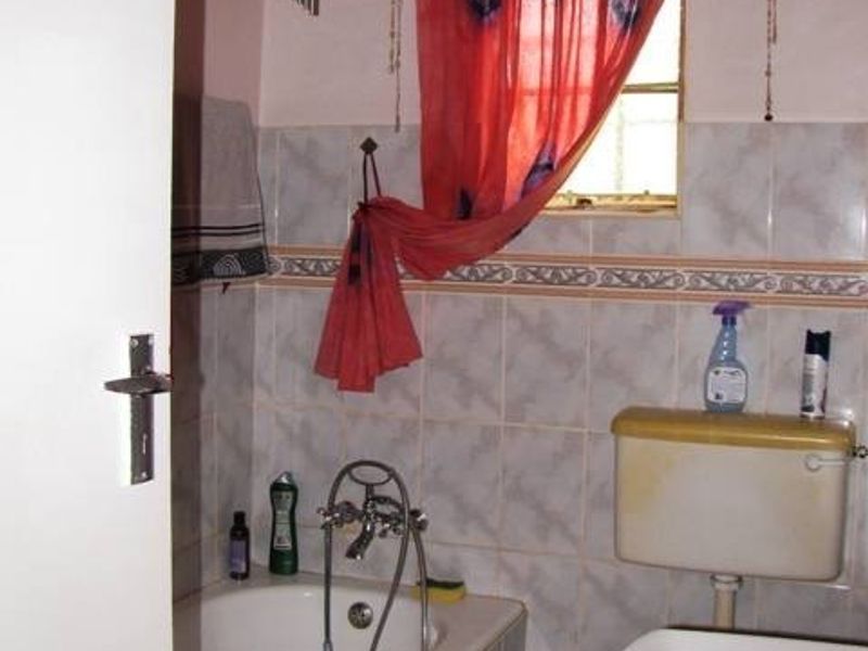 A dated bathroom featuring a bathtub with a handheld shower mixer, wall tiling, and a standard toilet cistern.