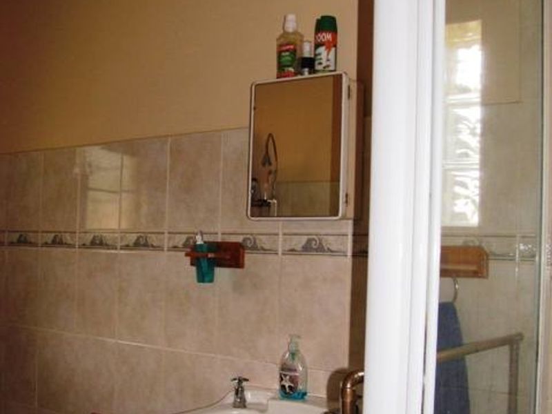 A functional bathroom featuring a wall-mounted basin, tiled splashback, medicine cabinet, and a shower enclosure with exposed plumbing.