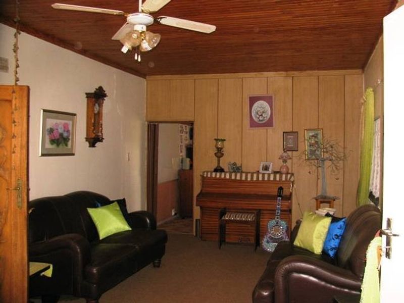 A living room featuring a timber ceiling, ceiling fan, and wood-paneled walls, offering a traditional aesthetic with potential for modernization.
