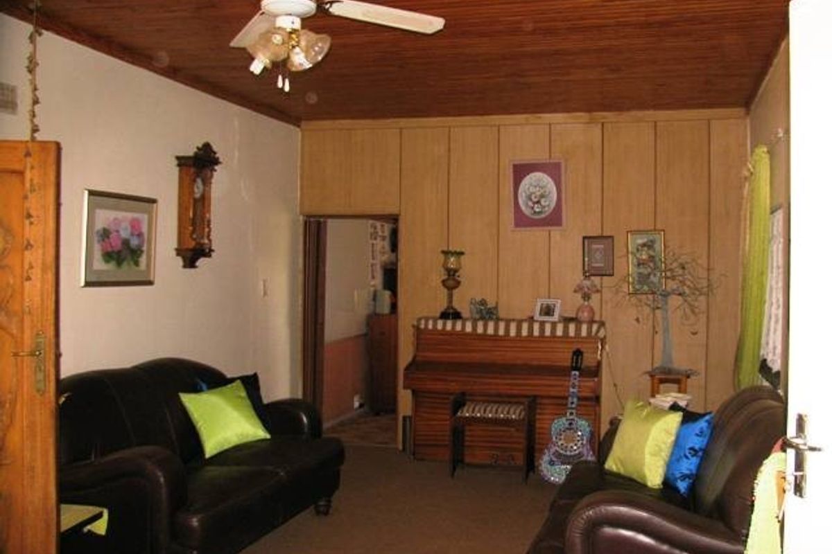 A living room featuring a timber ceiling, ceiling fan, and wood-paneled walls, offering a traditional aesthetic with potential for modernization.