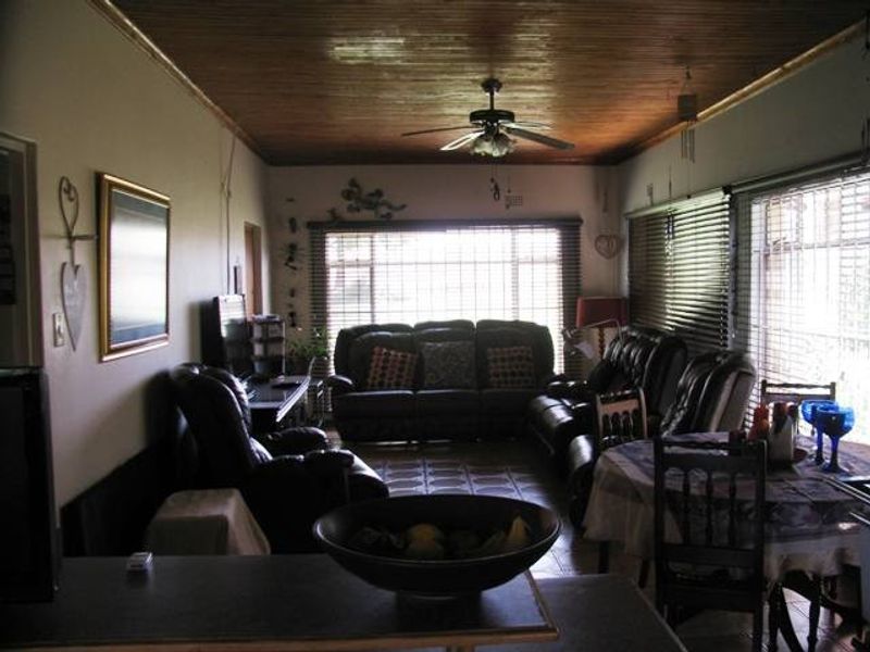 Open-plan living and dining area featuring a timber-clad ceiling, ceiling fan, and tiled flooring with large windows fitted with security bars and blinds.