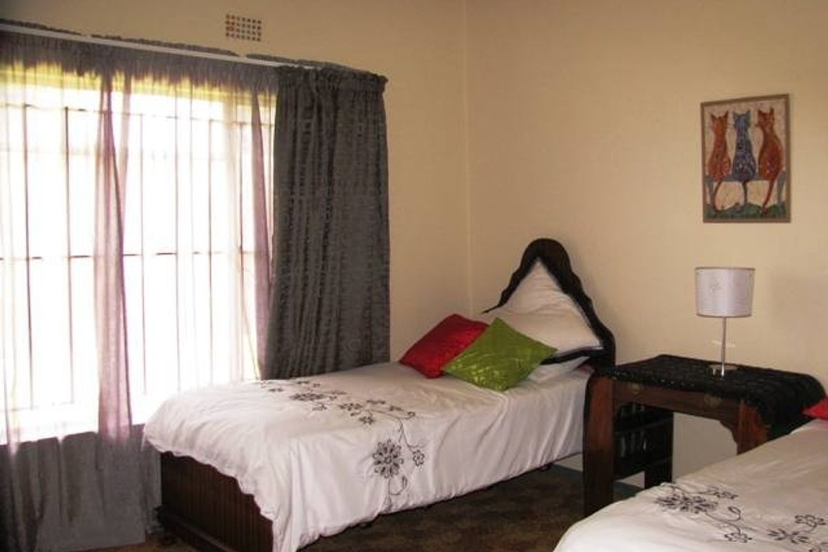 A functional bedroom featuring a large window with security bars and neutral wall finishes, providing a comfortable space for rest.