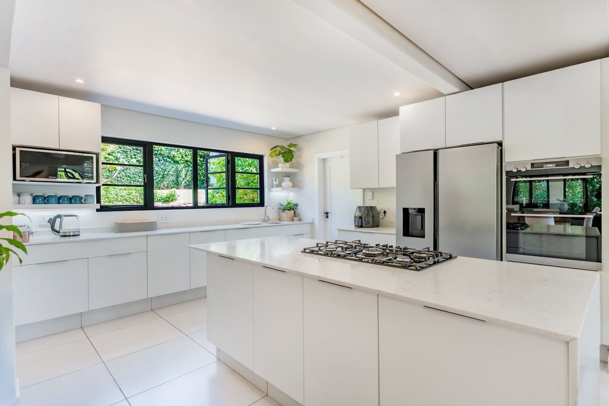 Modern, bright kitchen featuring white cabinetry, stone countertops, a central island with a gas hob, and high-quality built-in appliances.