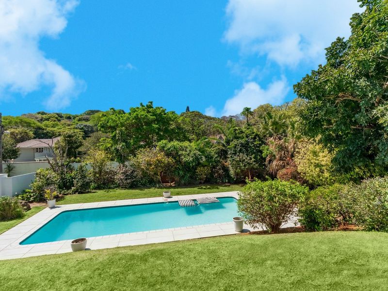 A well-maintained swimming pool set within a lush, landscaped garden, featuring a paved surround and mature greenery.