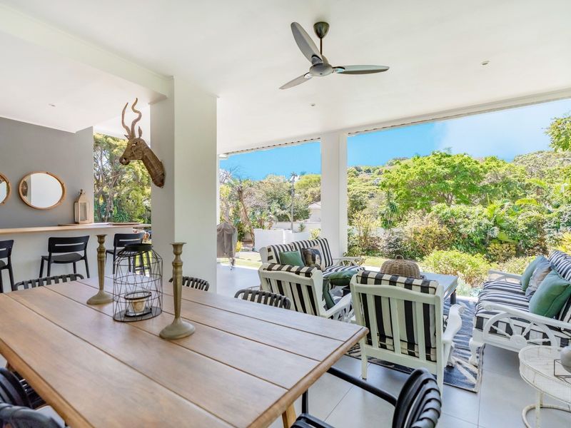 Spacious covered patio featuring a built-in bar counter, ceiling fan, and seamless flow to the garden, ideal for outdoor entertaining.