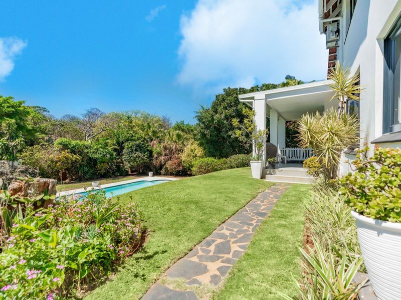 A well-maintained rear garden featuring a swimming pool, a stone-paved pathway, and a covered patio area attached to the main house.