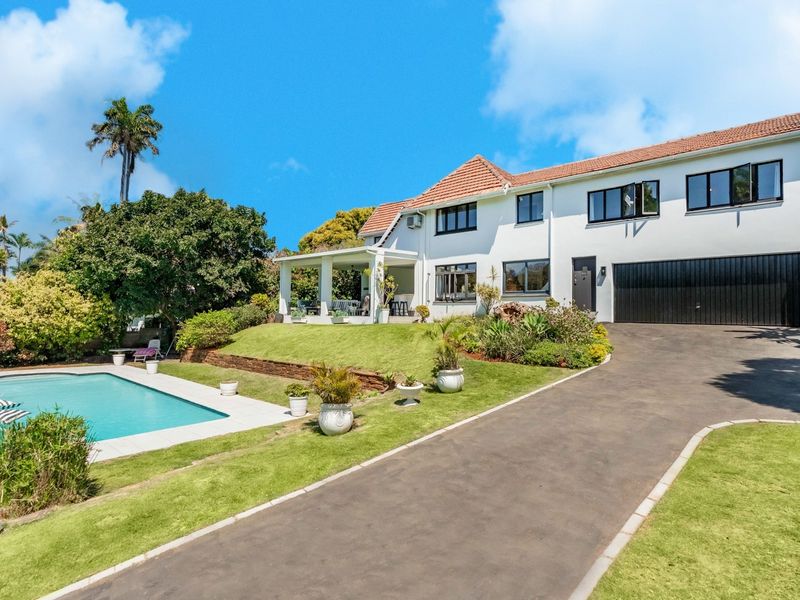 Rear view of a two-story residence featuring a swimming pool, covered patio, landscaped garden, and an attached double garage with a paved driveway.