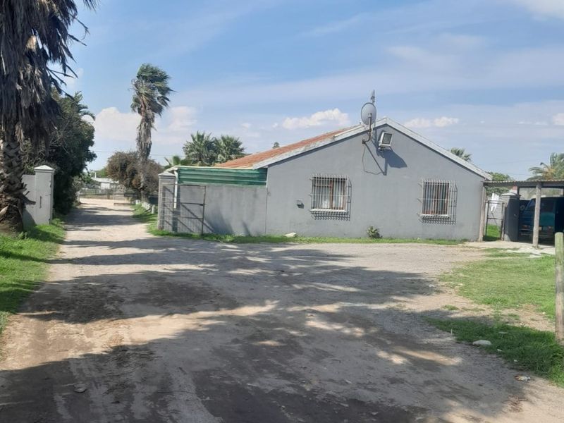Exterior view of the property featuring a grey facade, security bars on windows, and an unpaved driveway area.