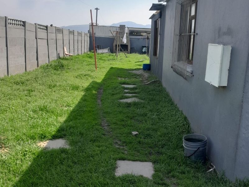 Rear garden area featuring a precast concrete boundary wall, a built-in outdoor braai, and a lawn with paved stepping stones.