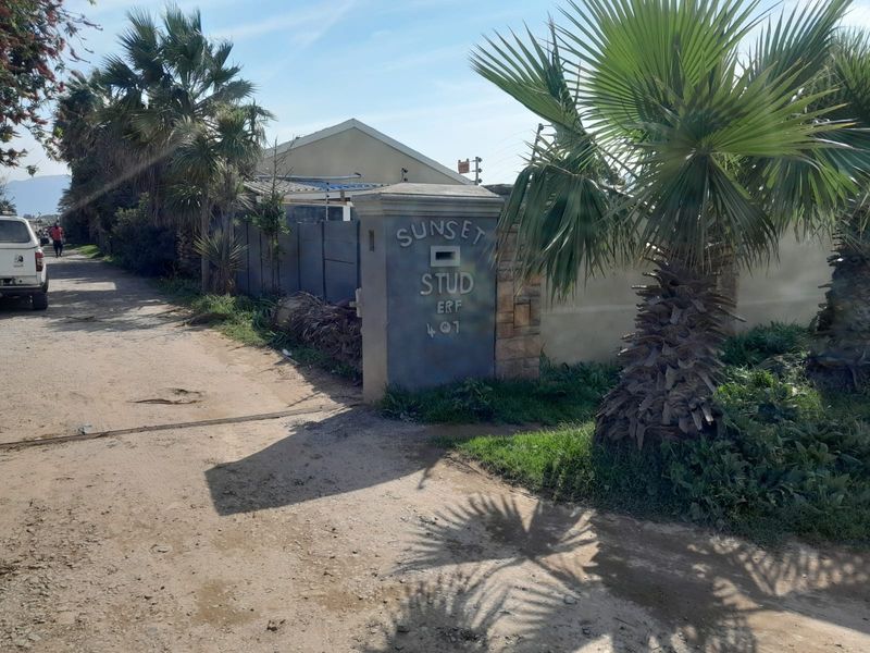 Front entrance view of the property featuring a boundary wall, entrance pillar, and unpaved access road.
