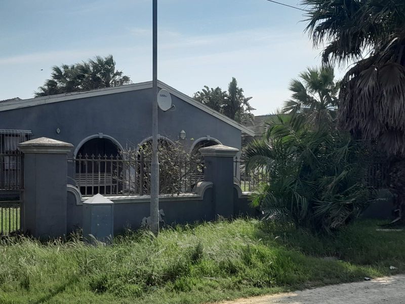 Front view of a residential property featuring a boundary wall with metal fencing, arched porch details, and established garden area.