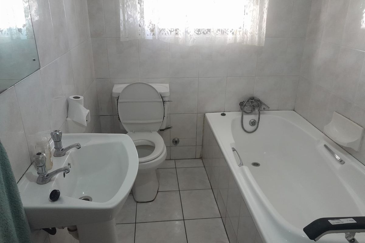 A functional bathroom featuring a pedestal basin, standard toilet, and a bathtub with wall-to-wall ceramic tiling.