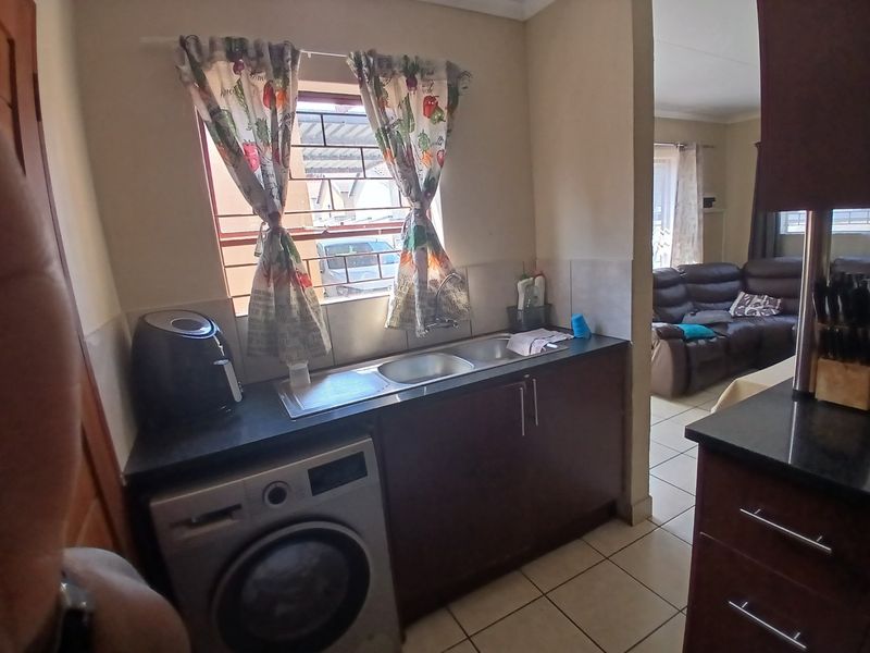 A functional scullery area featuring built-in cabinetry, a stainless steel sink, and tiled flooring, providing a practical space for laundry and kitchen prep.