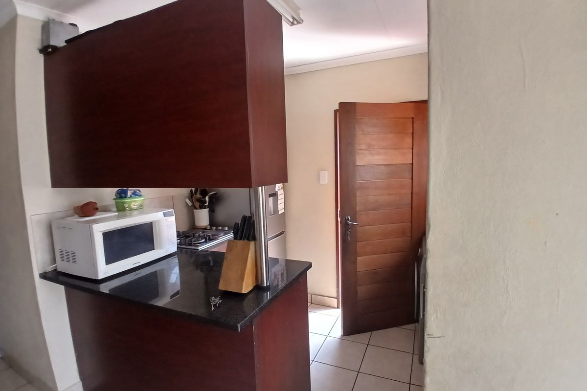 A functional kitchen featuring dark wood cabinetry, granite countertops, a gas hob, and tiled flooring, with a solid wood door leading to an adjacent area.