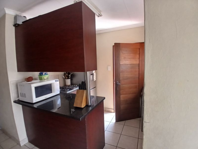 A functional kitchen featuring dark wood cabinetry, granite countertops, a gas hob, and tiled flooring, with a solid wood door leading to an adjacent area.