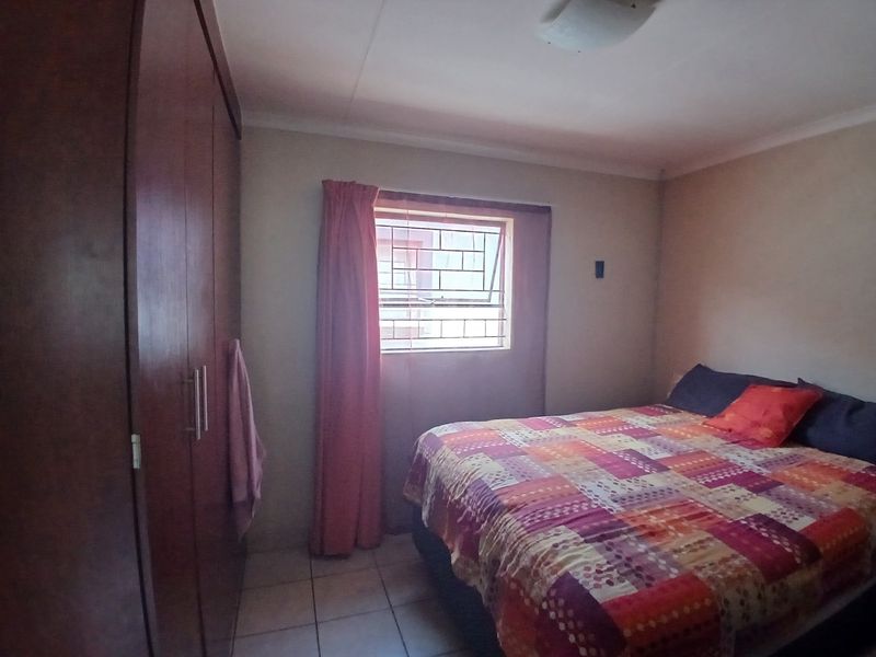 A functional bedroom featuring tiled flooring, a built-in wardrobe, and a window fitted with security bars.