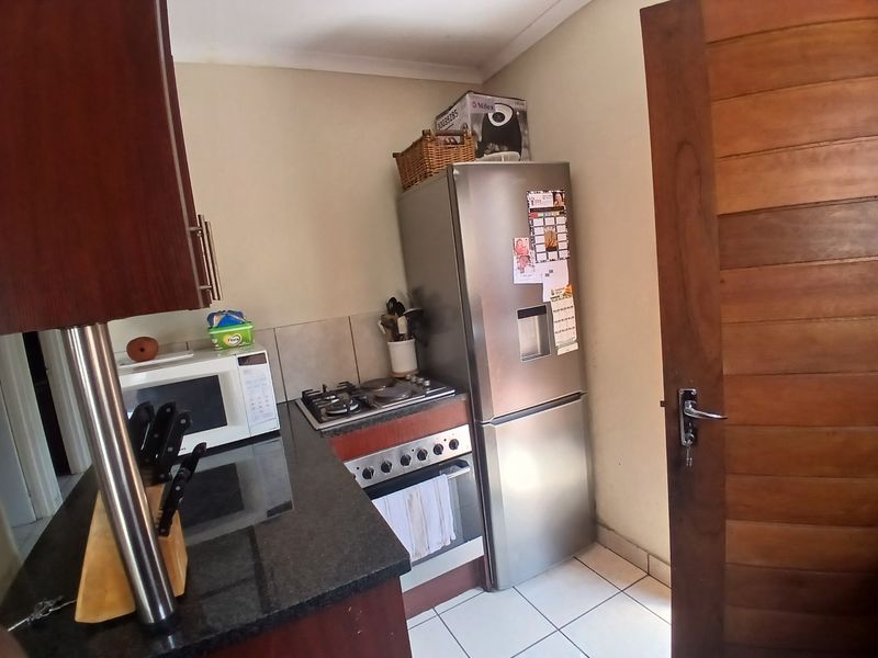 Compact kitchen featuring granite countertops, built-in oven with gas hob, tiled flooring, and wooden cabinetry.