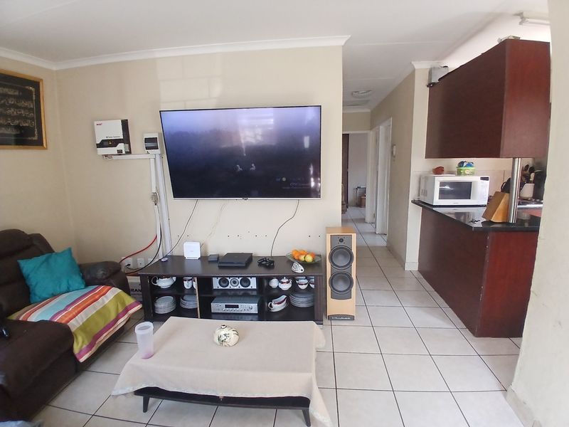 Open plan living area featuring tiled floors, built-in kitchen cabinetry with granite countertops, and wall-mounted solar inverter infrastructure.