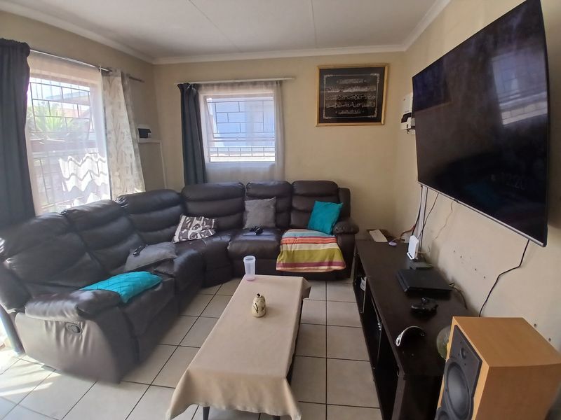 A functional living room featuring tiled flooring, wall-mounted television, and natural light through windows fitted with security bars.