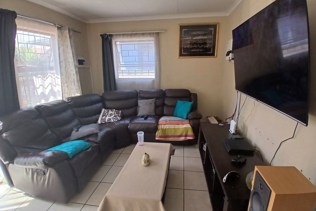A functional living room featuring tiled flooring, wall-mounted television, and natural light through windows fitted with security bars.