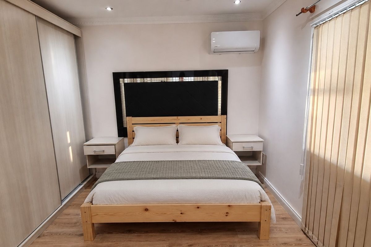 A well-maintained bedroom featuring laminate flooring, a large built-in sliding wardrobe, and a wall-mounted air conditioning unit.