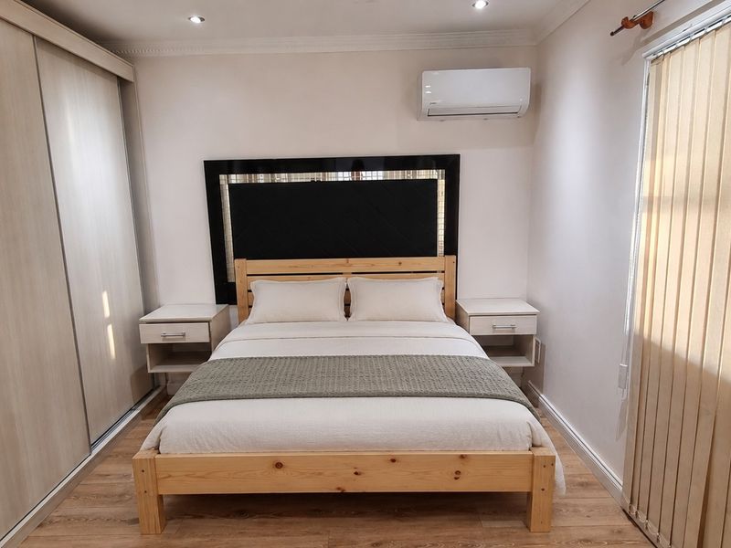 A well-maintained bedroom featuring laminate flooring, a large built-in sliding wardrobe, and a wall-mounted air conditioning unit.