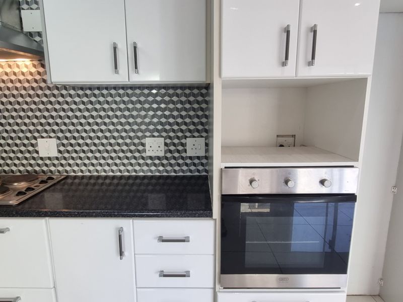 Modern kitchen featuring white gloss cabinetry, a geometric tile backsplash, built-in oven, electric hob, and stainless steel extractor fan.