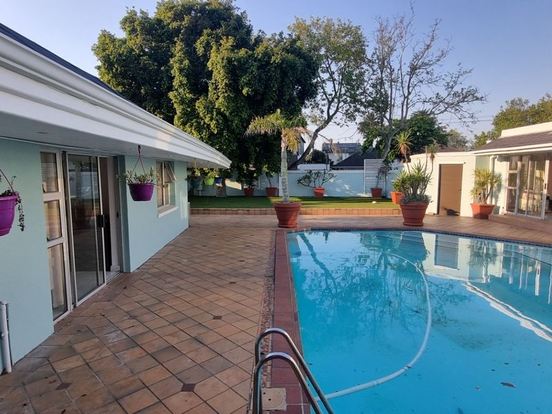 A spacious outdoor pool area featuring a tiled patio, swimming pool with ladder, and direct access to the cottage through sliding glass doors.