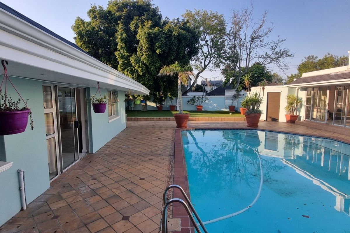 A spacious outdoor pool area featuring a tiled patio, swimming pool with ladder, and direct access to the cottage through sliding glass doors.