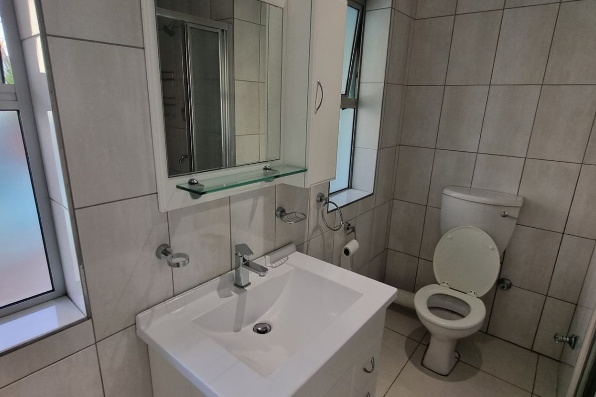A clean, modern bathroom featuring a vanity basin, toilet, and a glass-enclosed shower with neutral wall and floor tiling.