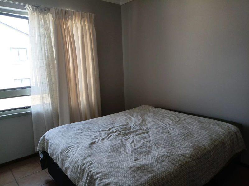 A simple bedroom featuring tiled flooring and a window with natural light, providing a neutral space ready for personalization.