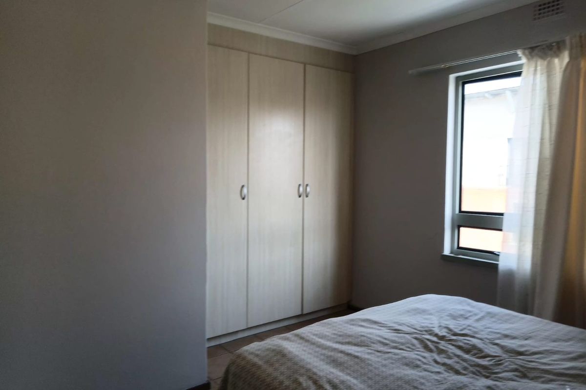 A bedroom featuring built-in cupboards, tiled flooring, and a window allowing natural light.