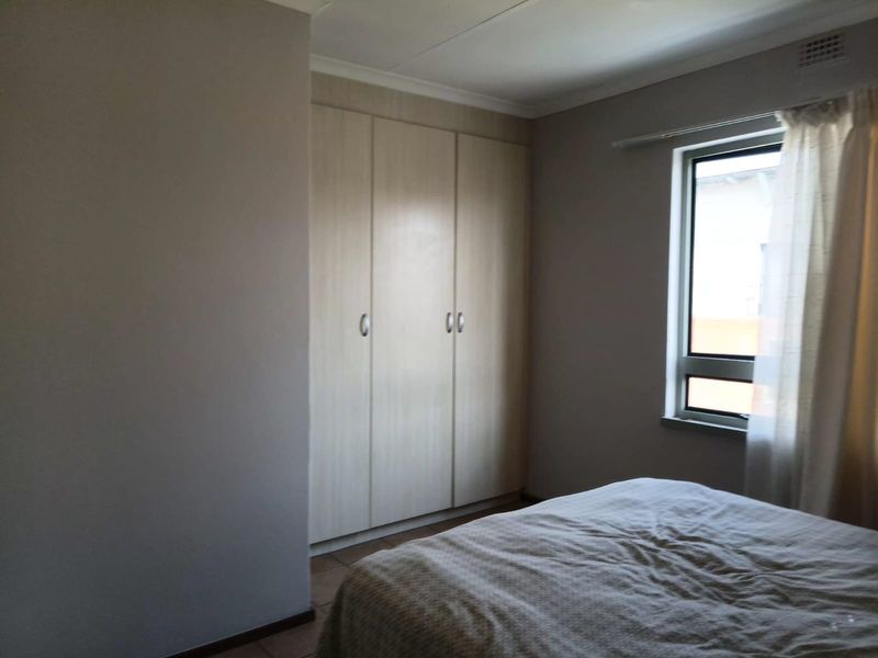 A bedroom featuring built-in cupboards, tiled flooring, and a window allowing natural light.
