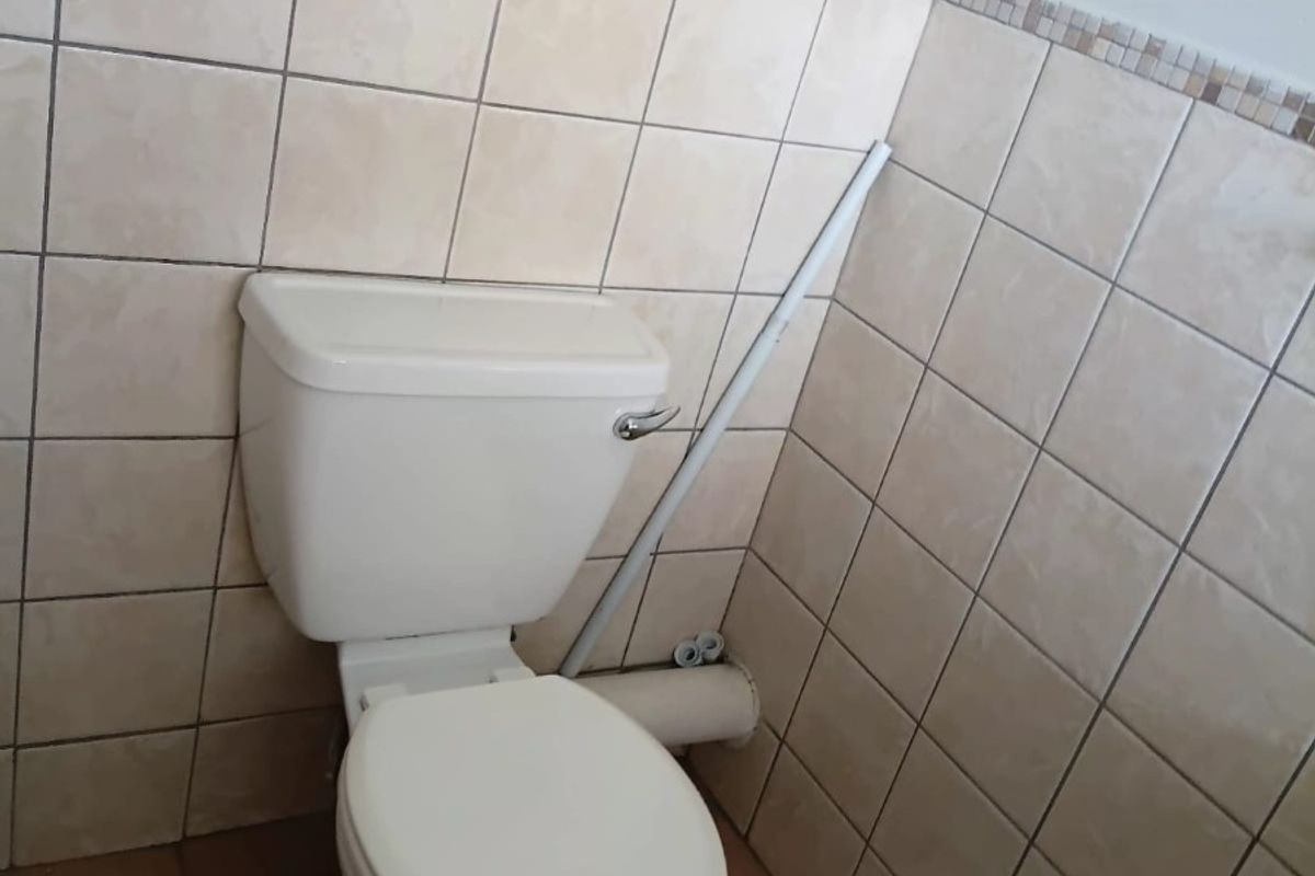 A compact bathroom featuring ceramic wall and floor tiling, a standard toilet, and a glass shelf, currently showing signs of dated finishes and exposed plumbing.