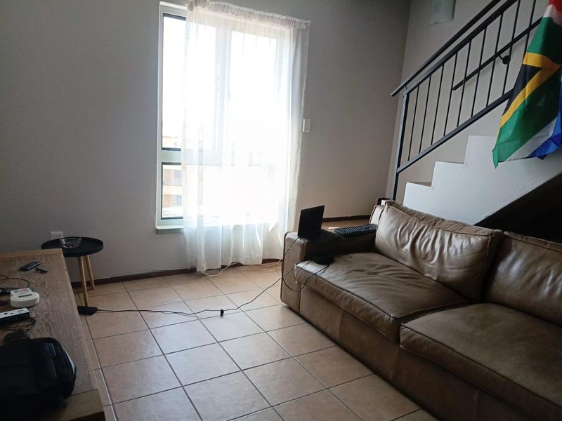 A living room area featuring tiled flooring, a staircase with a metal railing, and a large window providing natural light.