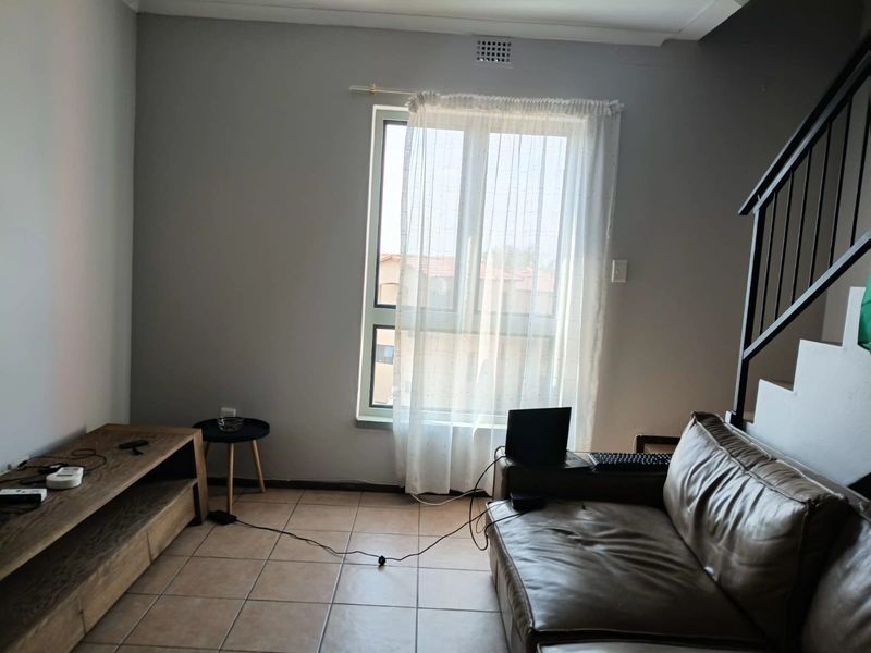 A living room area featuring tiled flooring and a staircase railing, with natural light entering through a window.