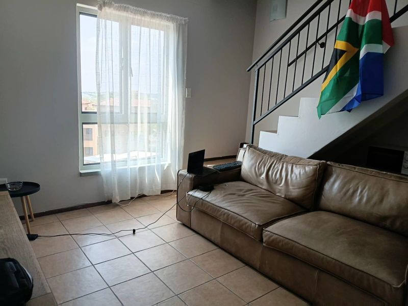 A living area featuring tiled flooring, a large window providing natural light, and an internal staircase with a metal balustrade.