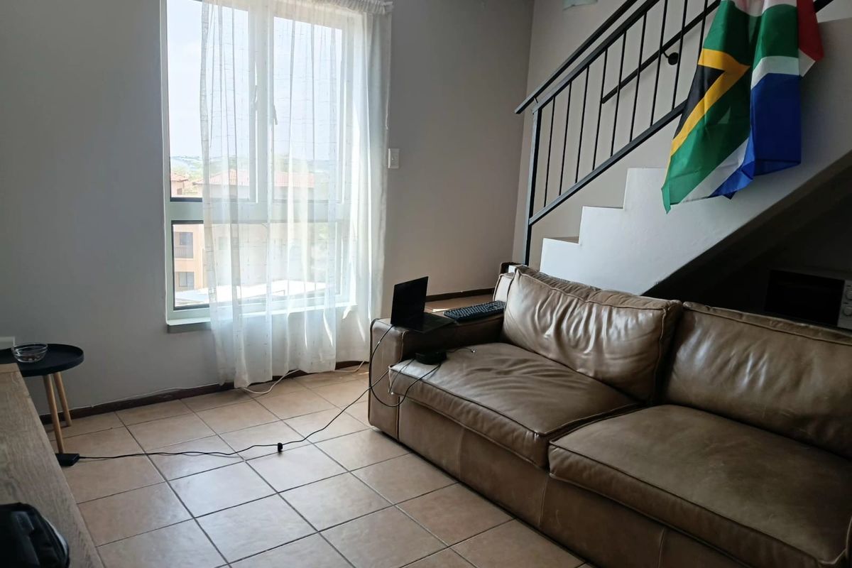 A living area featuring tiled flooring, a large window providing natural light, and an internal staircase with a metal balustrade.