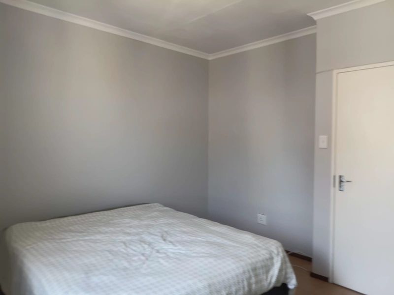 A simple, neutral-toned bedroom featuring clean walls, cove cornicing, and standard interior door access.