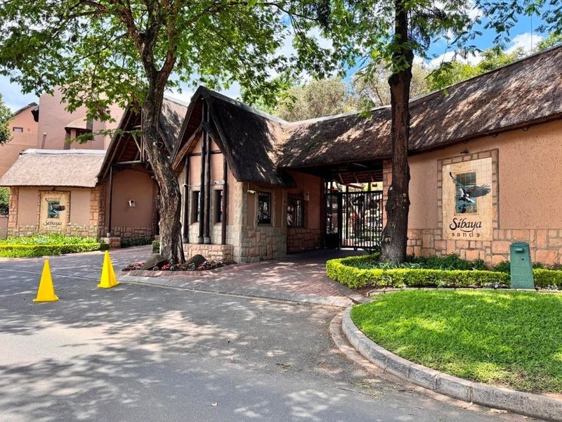 The main entrance and security gatehouse of Sibaya Sands, featuring traditional thatched roofing, stone facade detailing, and well-maintained landscaped surroundings.