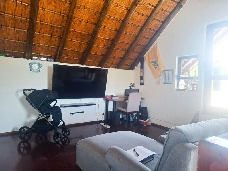A living room featuring a distinctive exposed thatch roof with timber rafters and dark wood flooring, creating a rustic atmosphere.